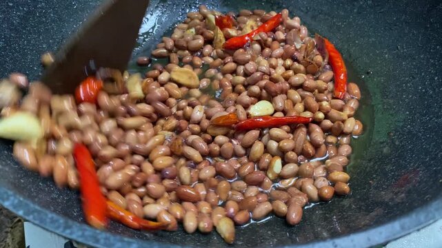 Peanuts are fried in a pan with garlic and curly red chilies; these peanuts are the basic ingredient for making pecel or gado-gado sauce.