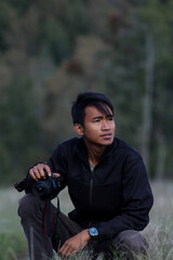 Fototapeta premium Young male photographer crouching outdoors holding digital slr camera equipment