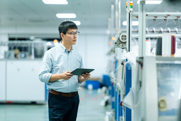 Engineer in factory workshop holding tablet to inspect textile machinery