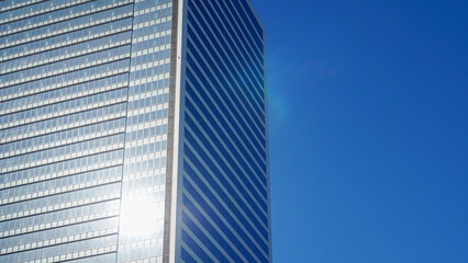 雲一つない青い空の下で太陽の光を反射して輝く近代的な高層ビルのガラス外壁
