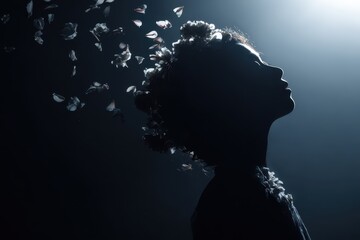 Girl with flowers in hair stands in shadow with petals floating around her in a dark setting during an artistic moment