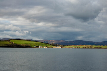 Obraz premium The other side of the bay with houses, the mountains are darkened by clouds, Whiddy island, West Cork, Ireland