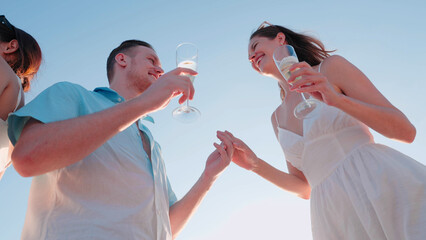 A happy romantic couple toasts with champagne against a clear blue sky on a luxury yacht. Low-angle...