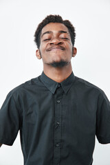 Fototapeta premium Young black man with dark skin wearing black shirt posing with confident smile and closed eyes on white background. Portrait of African ethnicity male with short hair and facial hair.