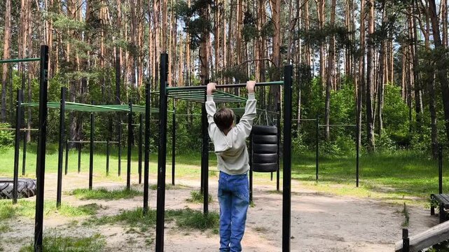 Sports and Outdoors Training. Young Boy Training in Sportsground and Doing Pull Ups on Bars. A teenager is doing pull-ups in the park