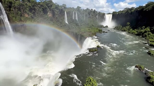 People watching massive Iguazu falls with vibrant rainbow at Argentine border as water crashes down into river during day time