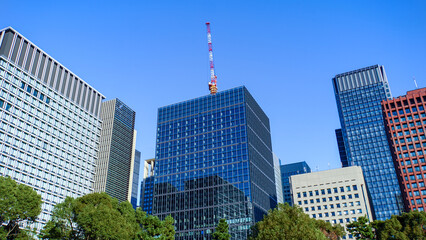 東京のビジネス街に建ち並ぶガラス外壁ビルと建設工事中のクレーン