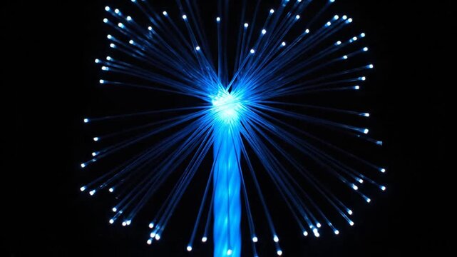 A mesmerizing close-up video showcases a bundle of blue illuminated fiber optic cables expanding and contracting in a dazzling, starburst pattern against a pure black background, simulating abstract 