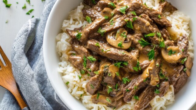 Creamy Mushroom Beef Stroganoff Served Over Steamed Rice with Fresh Parsley Garnish and Wooden Fork on Stylish Tablecloth