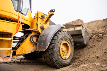 Yellow wheel loader moving sand at construction site