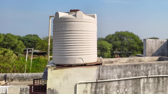White plastic water storage tank installed on a concrete rooftop of a house under a clear blue sky