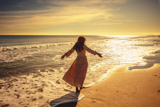 Seascape on a sunny day. A young woman with long blond hair walks on the beach. Happy woman in a long, flattering dress on the seashore