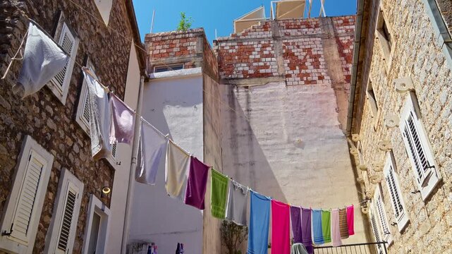 An authentic Mediterranean street scene in Petrovac, Montenegro, where beach towels hang out on clothesline to dry against a traditional stone building. It captures the charming everyday life and summ