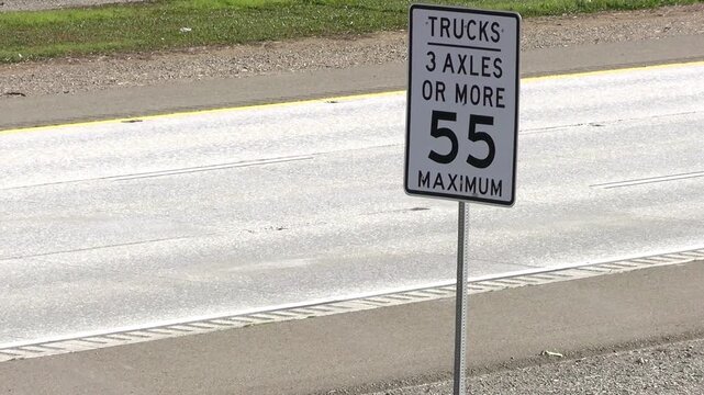 Truck speed limit sign (55mph)  on freeway with passing big rigs.