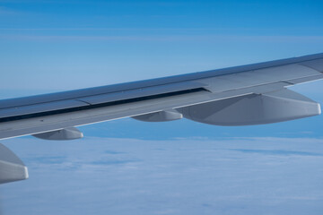 Airplane wing stretches over a soft cloud layer under a clear blue sky, captured mid-flight,...