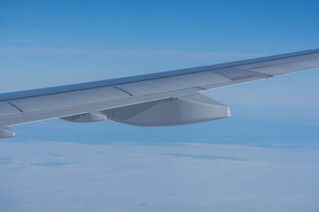 Obraz premium Airplane wing stretches over a soft cloud layer under a clear blue sky, captured mid-flight, highlighting calm travel and high-altitude perspective.