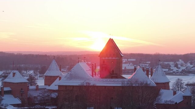 4K aerial drone lateral right shot of Trakai Island Castle, Lithuania, sun flare and rays disappear behind the main tower then reveal at winter sunset, cinematic medieval fortress footage