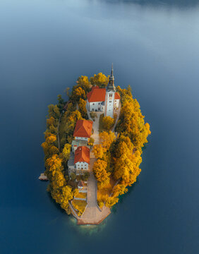 Aerial view of Lake Bled island surrounded by golden autumn foliage, featuring the iconic church rising above calm alpine waters in Slovenia