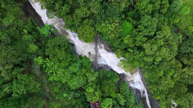 The image showcases Bambarakiri Ella Falls, a picturesque 3-meter waterfall near Rattota in Matale, Sri Lanka, surrounded by lush evergreen forest and featuring a charming suspension bridge