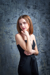 Fototapeta premium A beautiful woman in a black camisole poses for the camera against a blue background. She has a slender body.