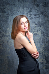 Fototapeta premium A beautiful woman in a black camisole poses for the camera against a blue background. She has a slender body.