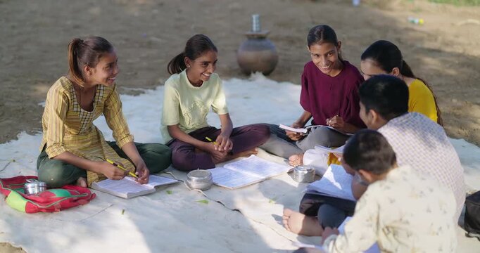 Indian villager girl boy sitting on mat do study read book outdoor rural area ground place. Happy group child hold pencil writing notes talk gossip enjoy desi life new day outside open class field