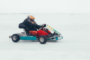 Professional racer in helmet and warm gear driving fast go kart on white snowy frozen river track during intense winter motorsport competition while performing high speed drift at outdoor circuit.