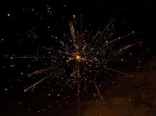 Firework Explosion Against Dark Night Sky ,Bright Orange and Yellow Sparks Radiating in Starburst Pattern with Trailing Bursts and Faint Clouds