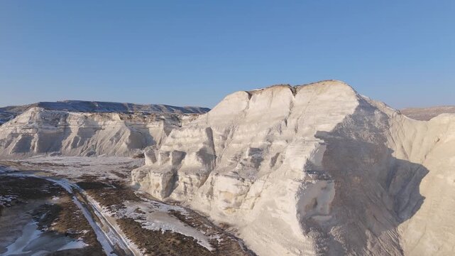 4K drone footage of massive white chalk cliffs formed on the ancient Tethys Ocean seabed. Aerial winter landscape of Akespe Canyon in Mangystau, Kazakhstan, with clear sky and striking geological text