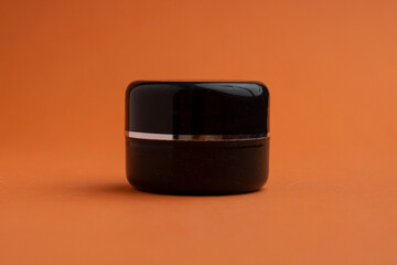 Dark round jar with a lid for skin and hair care cosmetics isolated on a orange background. Plastic container, packaging for cream, gel, mask on a white background.