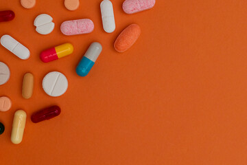 Various colorful pills and capsules form a frame, isolated on a orange background, copy space for text. Medical concept.