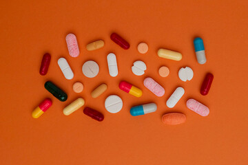 Various colorful pills and capsules form a frame, isolated on a orange background, copy space for text. Medical concept.