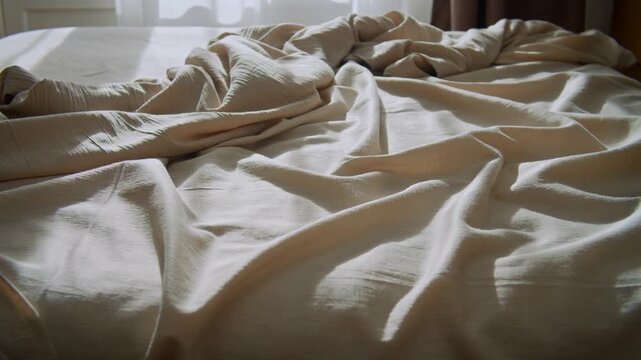 Unmade bed with rumpled white sheets in natural light.