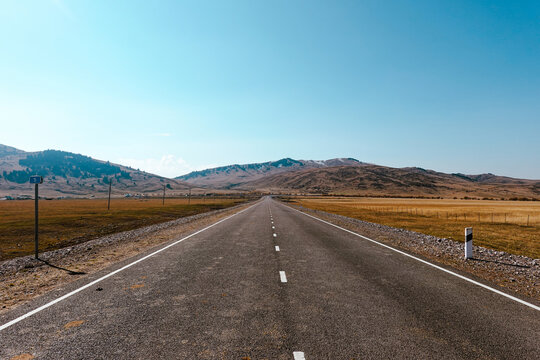 Empty road through vast grassland leading to mountains under clear blue sky