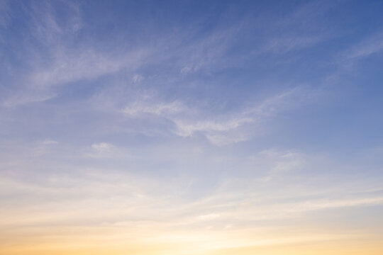 Beautiful sunset sky with orange clouds and blue gradient background,Vibrant sunset sky featuring soft wispy clouds illuminated by golden light, transitioning from deep blue to bright orange.