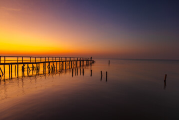 Obraz premium Golden Hour Silhouette of a Wooden Pier Over Calming Sea at Sunset,A serene and breathtaking sunset landscape featuring a long wooden pier stretching into the calm ocean. 