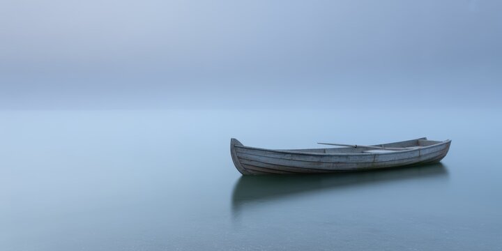 Tranquil wooden boat on calm misty lake at sunrise minimal serene blue landscape with copy space for peaceful meditation design