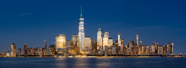 Panoramic view of New York City Lower Manhattan skyline at dusk with the Hudson River. Illuminated skyscrapers of the Financial District and World Trade Center © Francois Roux