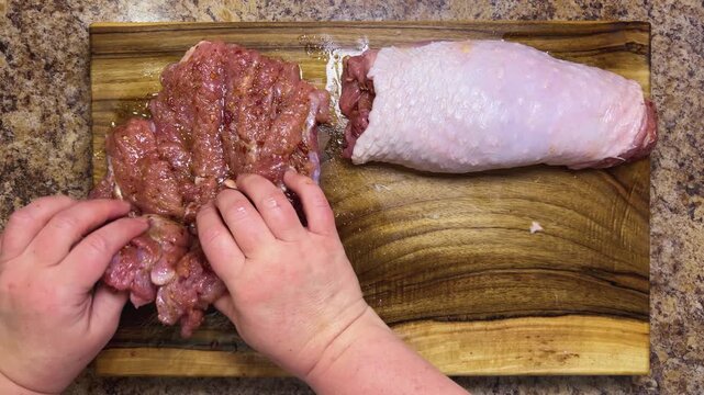 Preparing the turkey thigh for the roulade. The process: hand-roll the prepared piece of meat with spices on a wooden board.