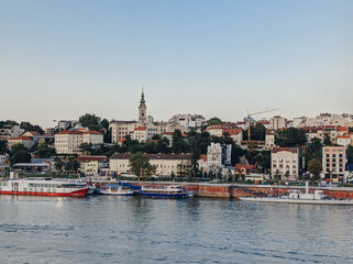 Fototapeta premium View of Belgrade city center from the Sava river with historic buildings, church tower and waterfront boats. European urban skyline with soft vintage tones