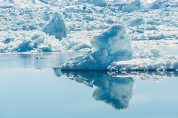 Icebergs and snow cover stones at Ilulissat Icefjord in Greenland during daytime with blue sky and water reflections