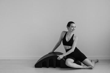 Obraz premium Black and white studio image features a young female performing controlled movements on curved Pilates barrel apparatus. Emphasis on equipment shape function support and balance 