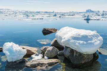 Snow covers stones along the water at Ilulissat icefjord in Sermeq Kujalleq, Qaasuitsup, Greenland during a clear day