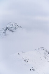 A line of climbers moves along a high ridge under a muted sky. The composition emphasizes journey, scale, and the quiet determination of ascent.