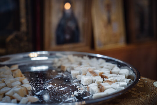 Consecrated bread antidoron on shiny silver platter close-up, against blurred icons in Orthodox church