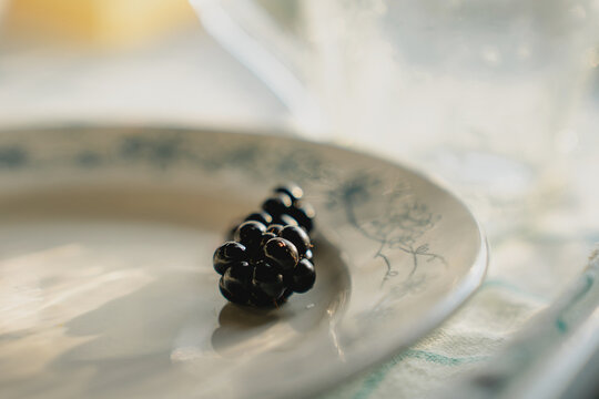Black ripe blackberry on white plate in summer sun, blurred light and shadow