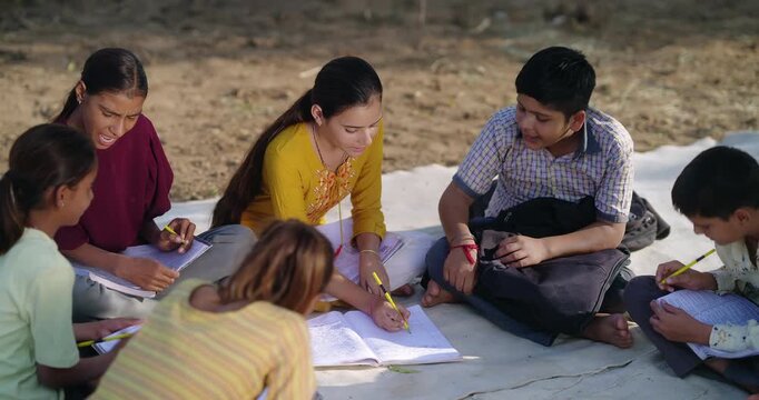Indian villager girl boy sitting on mat do study read book outdoor rural area ground place. Happy group child hold pencil writing notes talk gossip enjoy desi life new day outside open class field