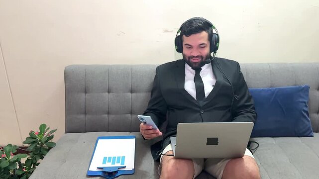 Businessman wearing a suit and shorts working on his laptop from the couch during a video call