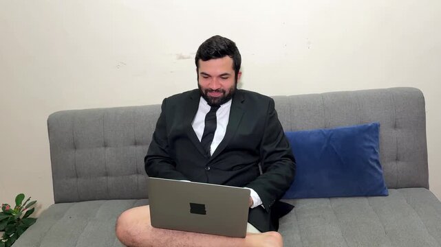 Funny businessman in a suit jacket with no pants attending a video conference call from his couch