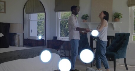 Holding hands couple smiling and facing each other in bedroom, wearing jeans and shirt with bed